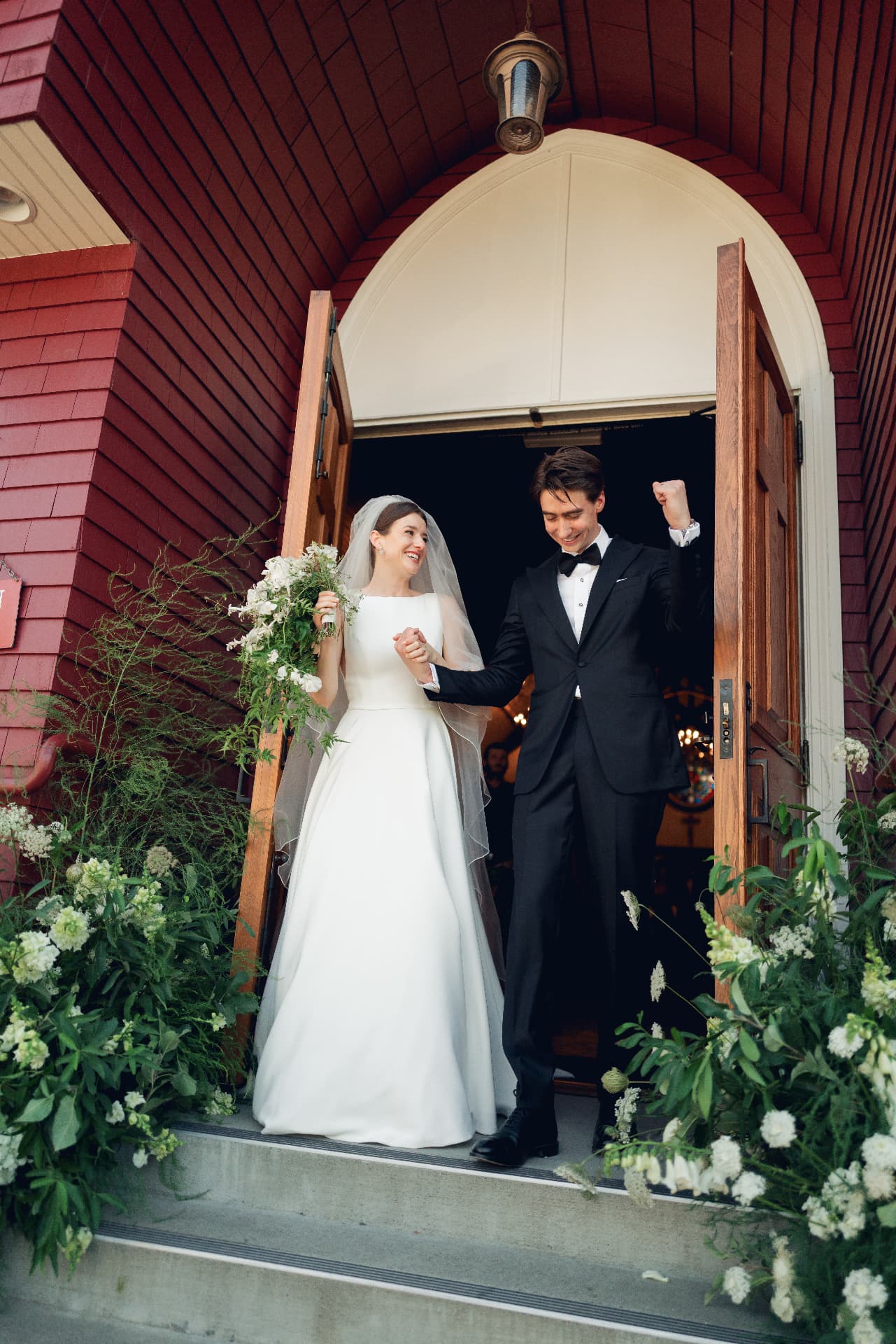 Newlyweds celebrating as they exit a chapel framed by white florals